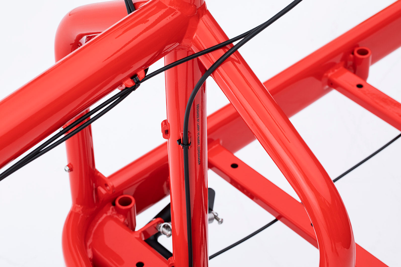 A closeup of the Bullitt X cargo bike frame in a bright red. Print on the steering tube reads "Designed by Larry vs Harry, Copenhagen" in small black lettering.
