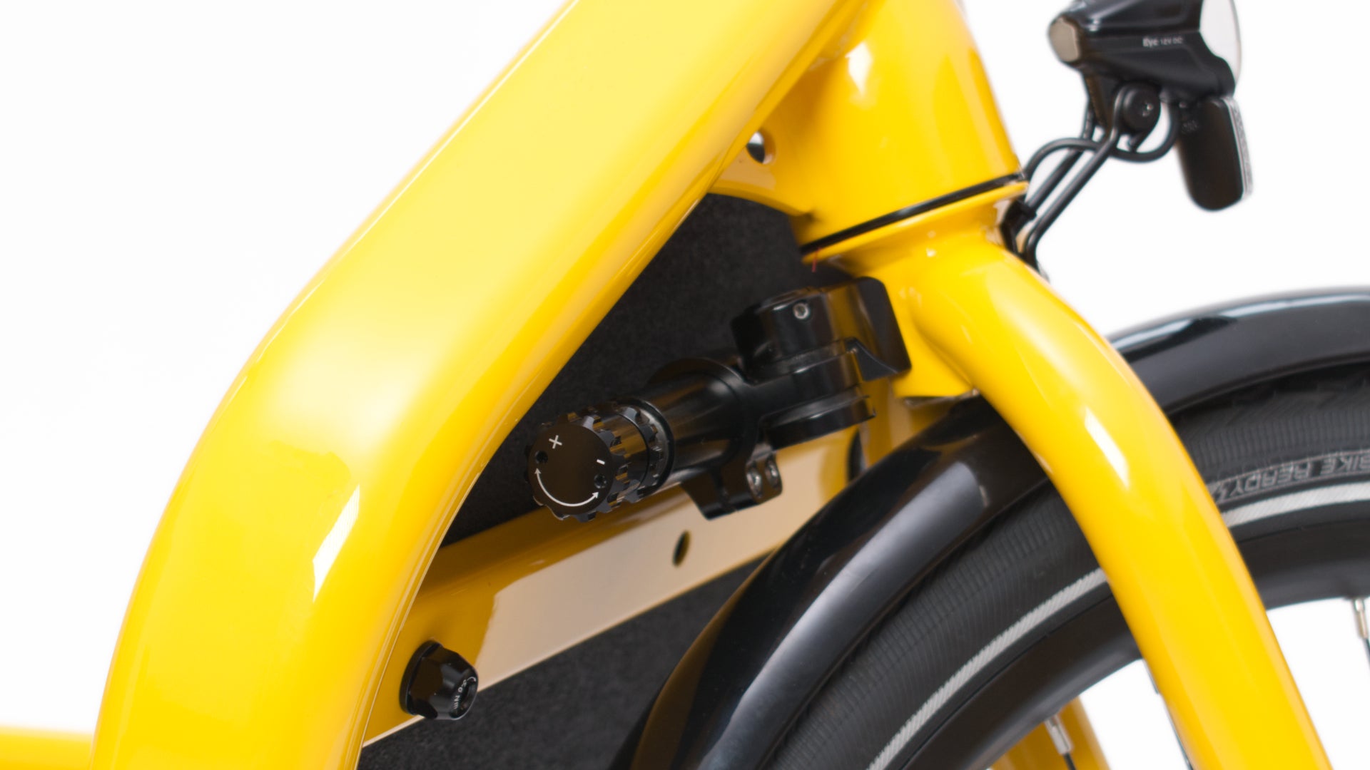 Closeup of a yellow Bullitt cargo bike front fork and headset, showing a hydraulic steering damper with a plus and minus dial at the end.
