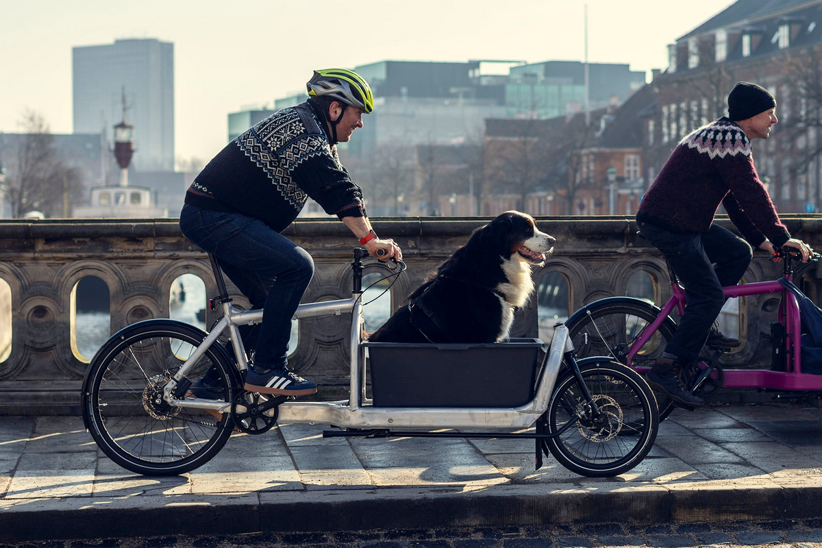 Two men riding Bullitt cargo bikes across a bridge in Copenhagen. One has a dog riding in front.