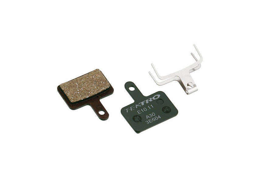 Two brakepads and retaining clip on a white background, one brakepad with the backside facing the camera. The backside is green with "Tektro", "E10.11", "A30" and "3E604" printed on it.