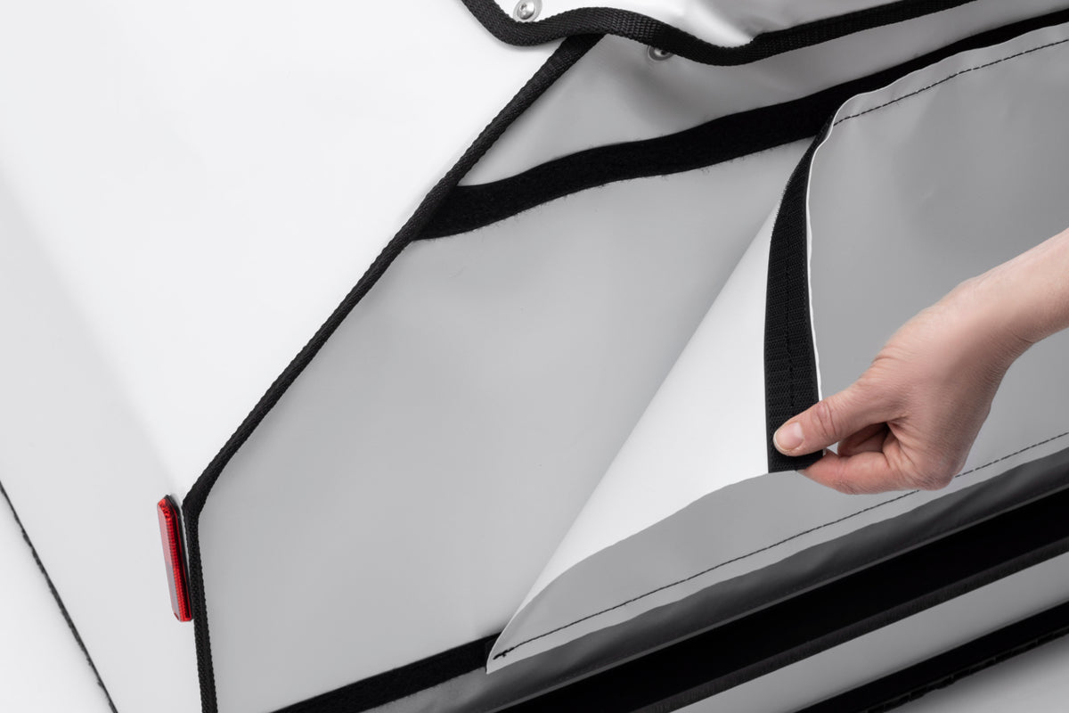A hand is removing the tarp panel on the side of the BagPRO box for Bullitt cargo bikes. The panel is attached with velcro.