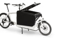 A white eBullitt cargo bike with a lidded black aluminium cargo box mounted on the cargo bed. The lid is open, with a hydraulic arm and the locking mechanism visible.