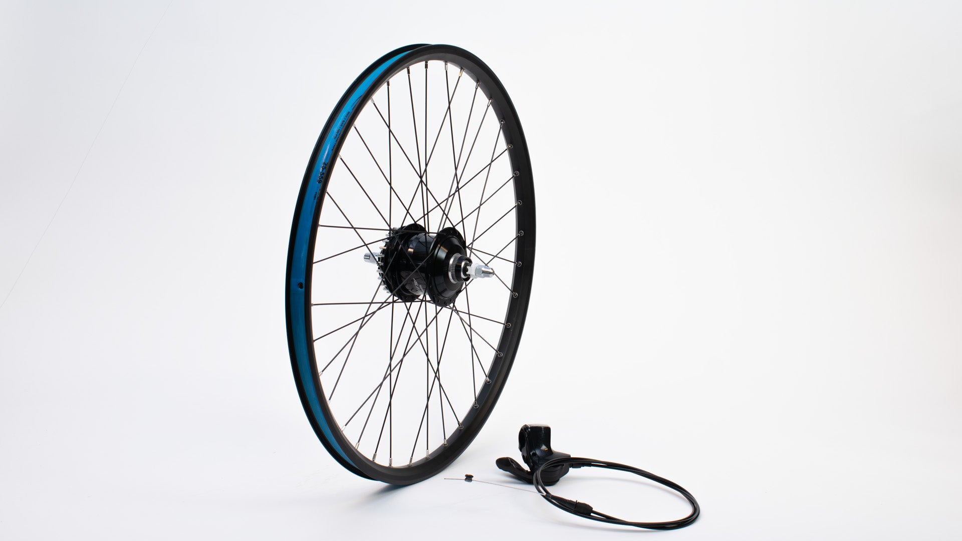 A 26" wheel without tyre standing on a white surface, a shifter lever with cable lying next to it.