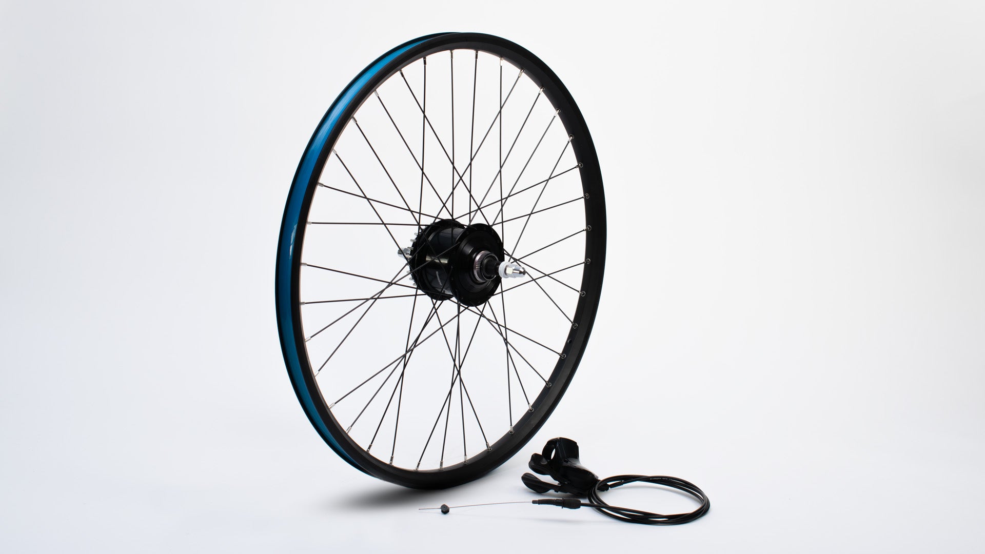 A 26" wheel without tyre standing on a white surface, a shifter lever with cable lying next to it.