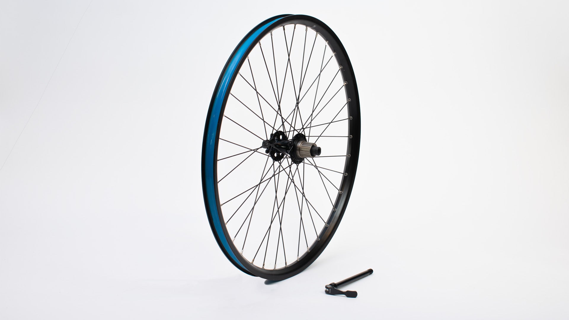 A 26" wheel without tyre standing on a white surface, a 142mm quick release axle lying next to it.