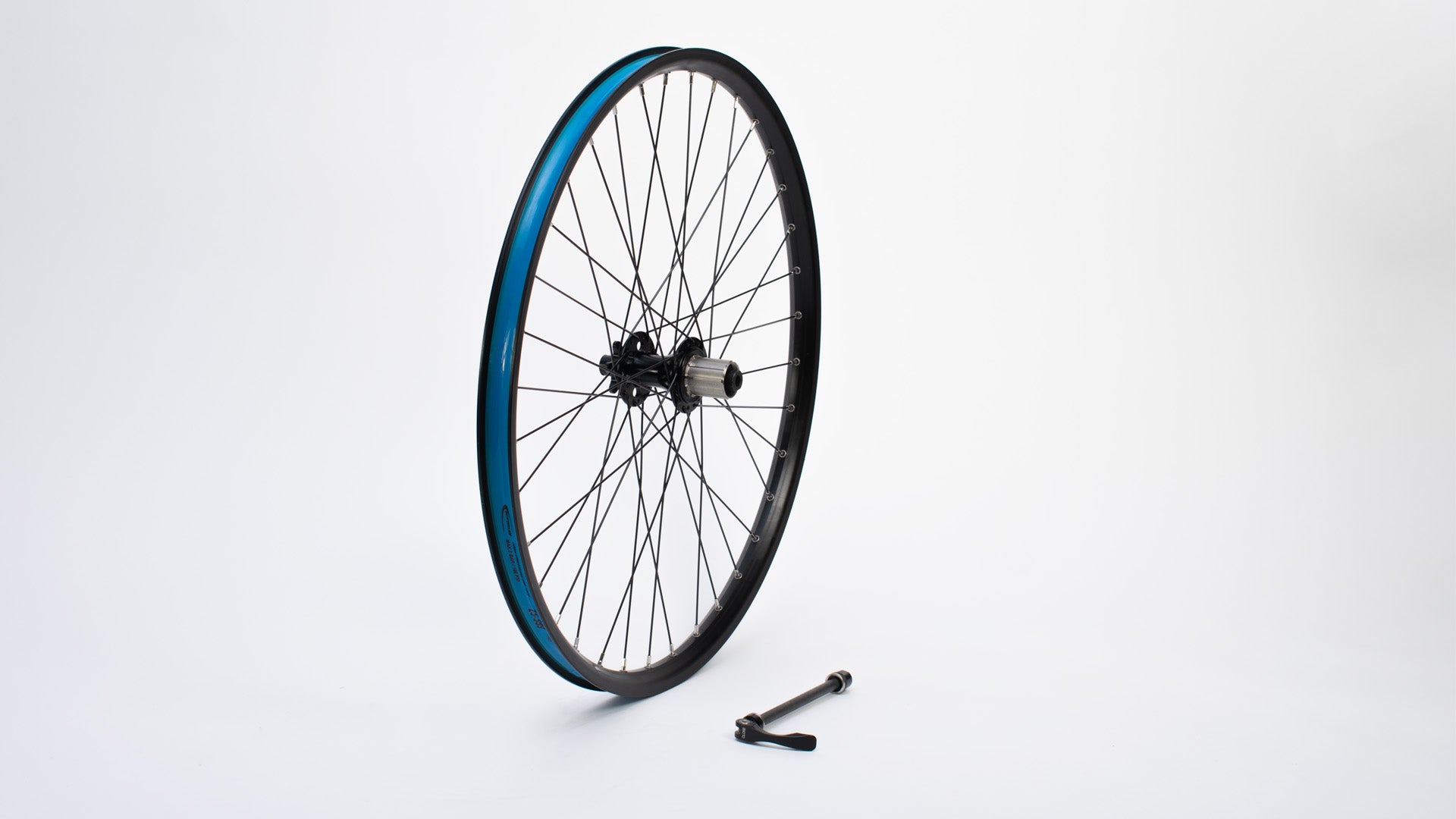 A 26" wheel without tyre standing on a white surface, a 135mm quick release axle lying next to it.