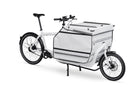 A white Bullitt cargo bike with a white cargo box in the front load area. The cargo box has a lid with a lock and plastic bumbers on the sides, corners and top, as well as reflexes in seveal places.