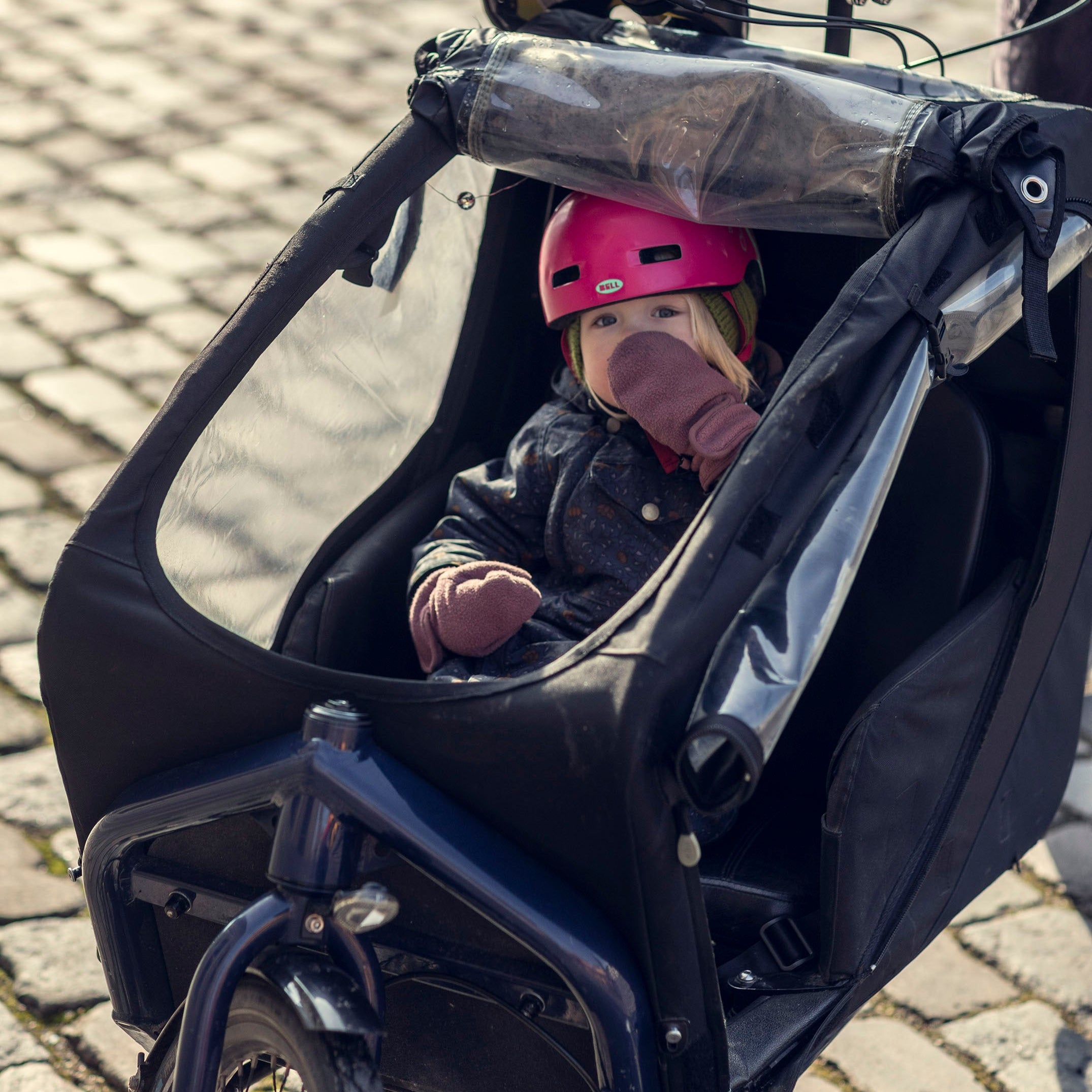 Cute little girl sitting in a Bullitt cargo bike children's seat, looking into the camera