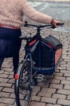 A woman is walking with a Moondog Bullitt cargo bike on cobblestones.