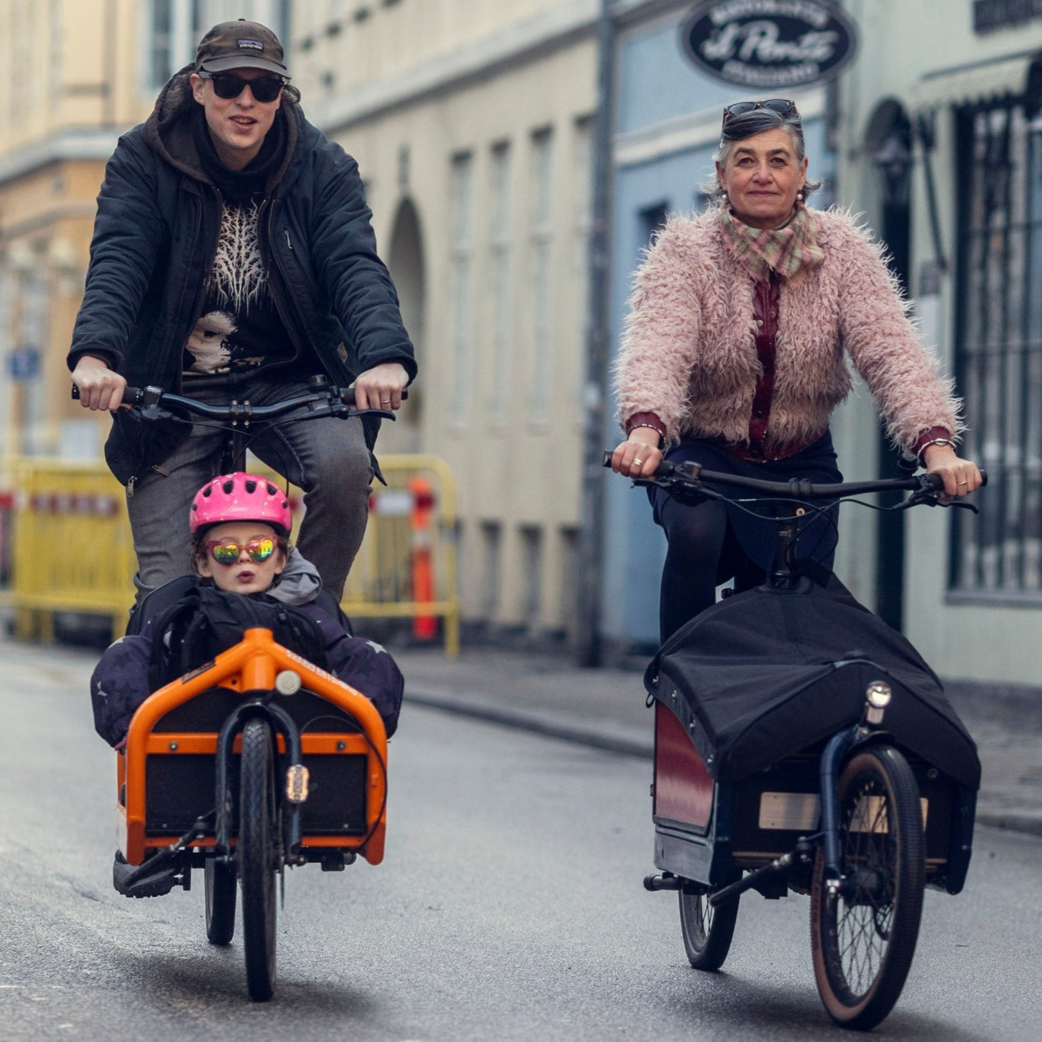 A man and a woman looking happy while biking on Bullitt cargo bikes in the street in Copenhagen, one with a child in the front