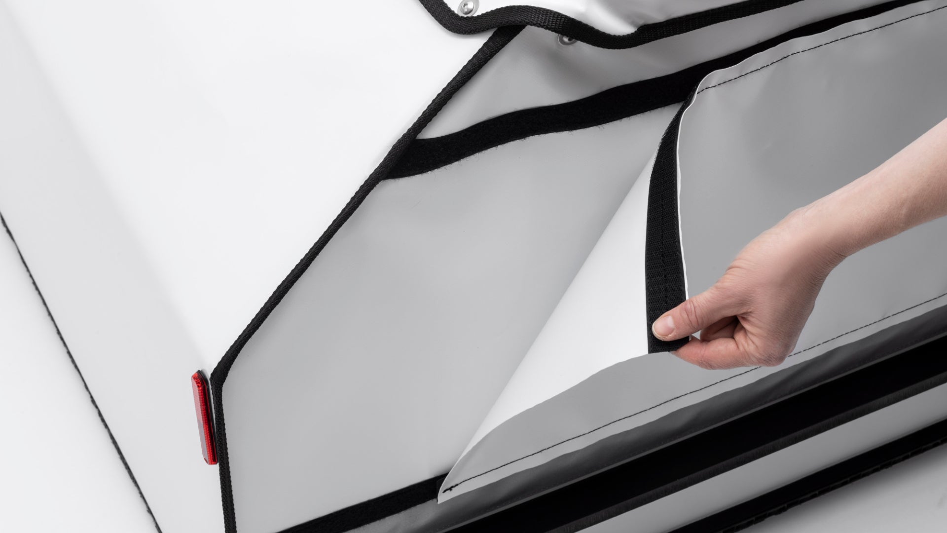 A hand is removing the tarp panel on the side of the BagPRO box for Bullitt cargo bikes. The panel is attached with velcro.