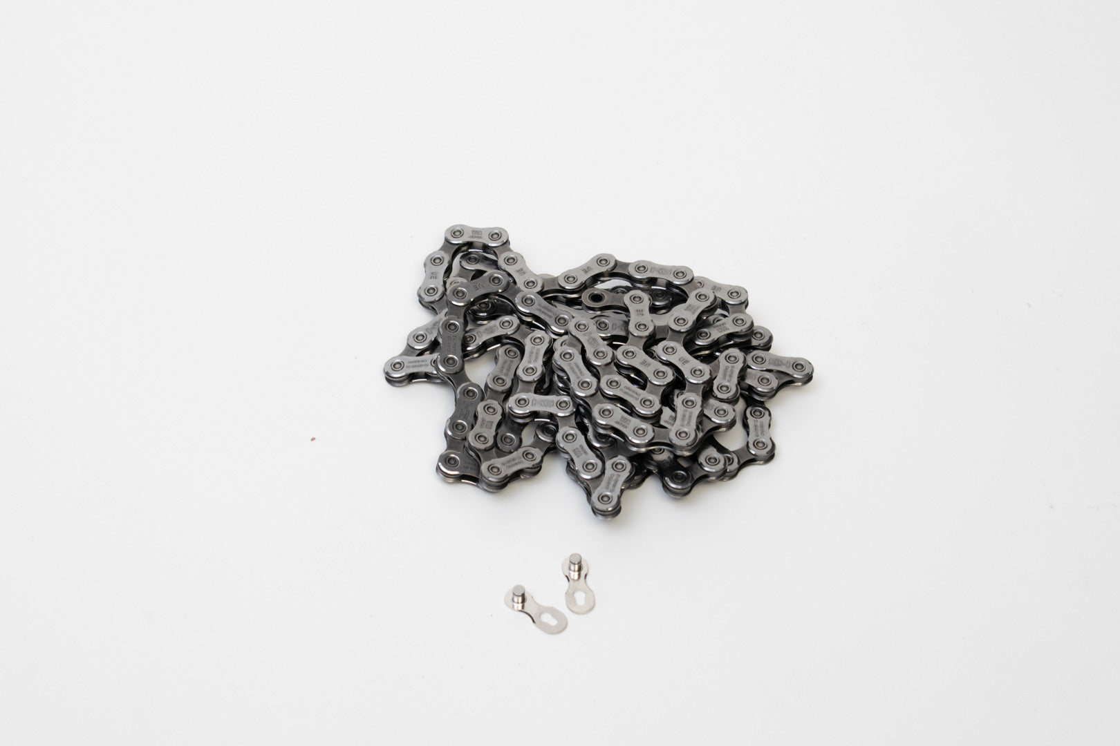 Shimano bike chain coiled up on a white surface with a Shimano quick link lying beside it