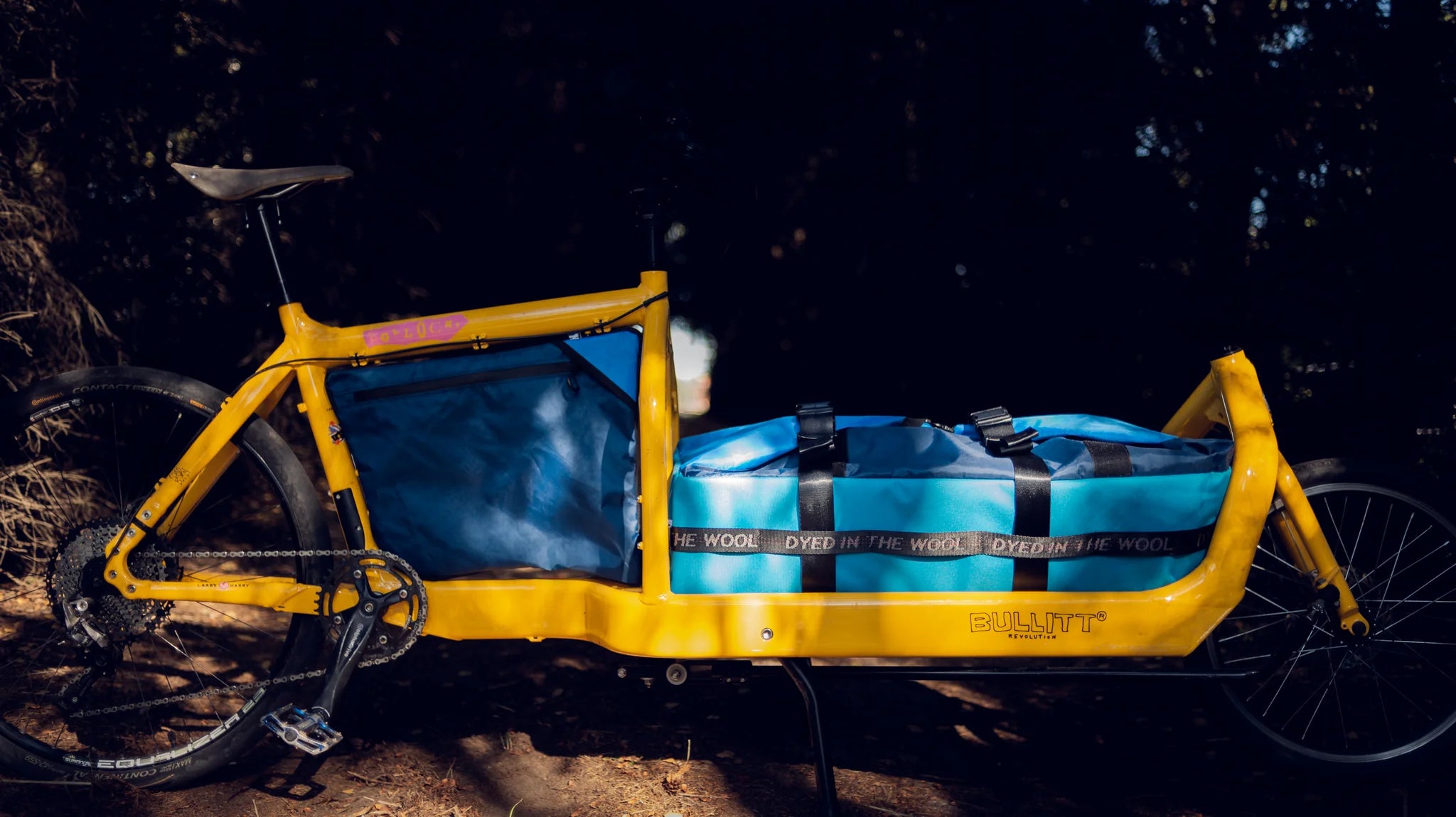 Yellow Bullitt cargo bike with blue and black bags parked in a forest