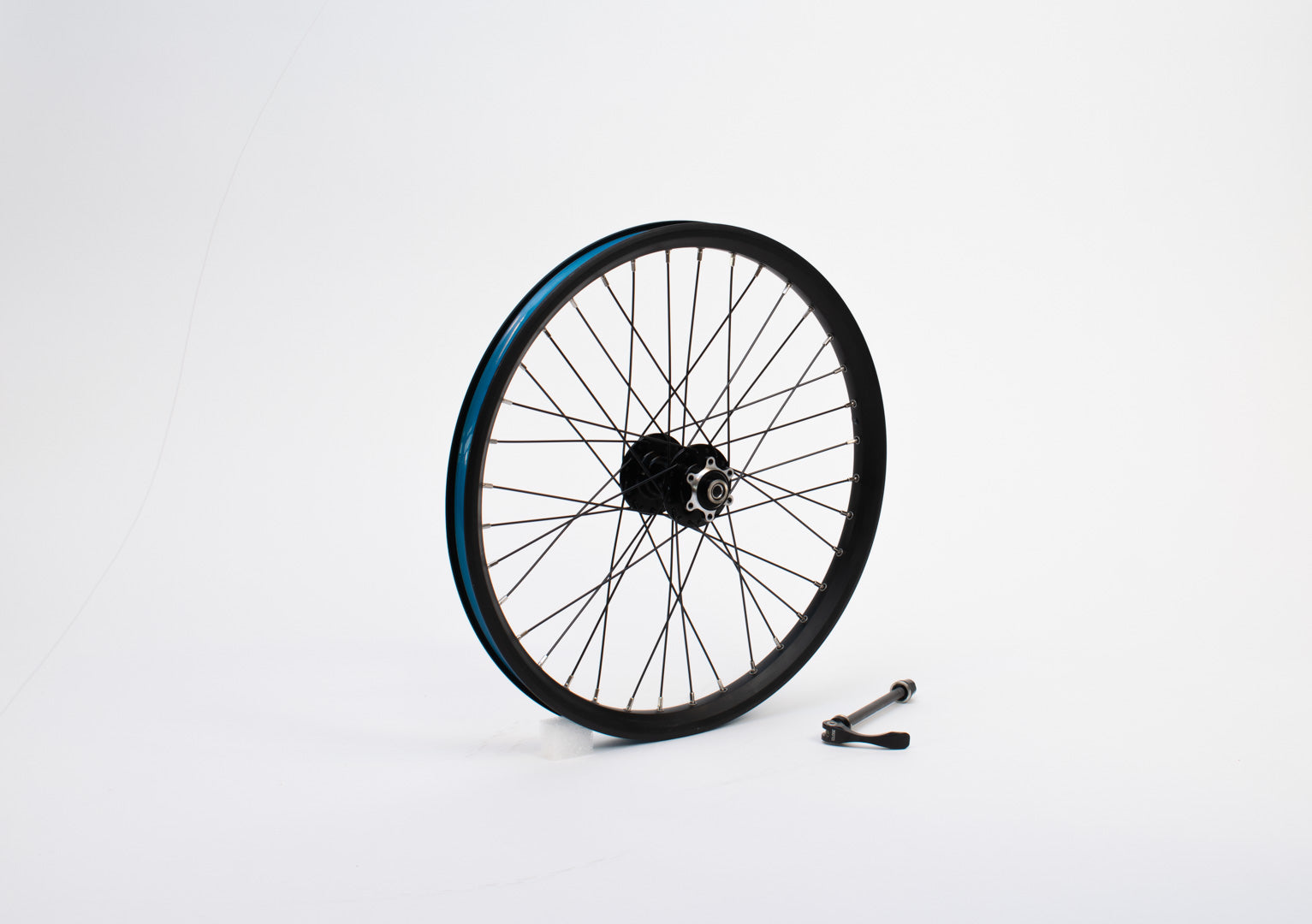 A 20" bike wheel without tyre, standing on a white surface. Beside it is an axle with quick release.